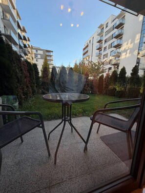 Un espace patio avec une table ronde et deux chaises, entouré d’un jardin et bordé par des immeubles d’habitation.