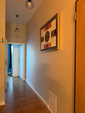 A hallway with wooden flooring, a wall-mounted artwork, and a door on the right. - Lumina Premium 2BR Apt w/ Parking I AC (Warszawa)