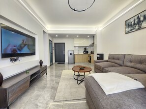 A modern living room with a flat-screen TV, a sofa, a coffee table, and a kitchen in the background. - Cozy 1-bedroom apartment in awesome Nairobi with gym and pool- Kilimani (Nairobi)