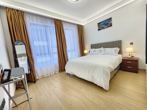 Une chambre d’hôtel avec un lit, des lampes de chevet, une table de chevet, un miroir et une fenêtre avec des rideaux.