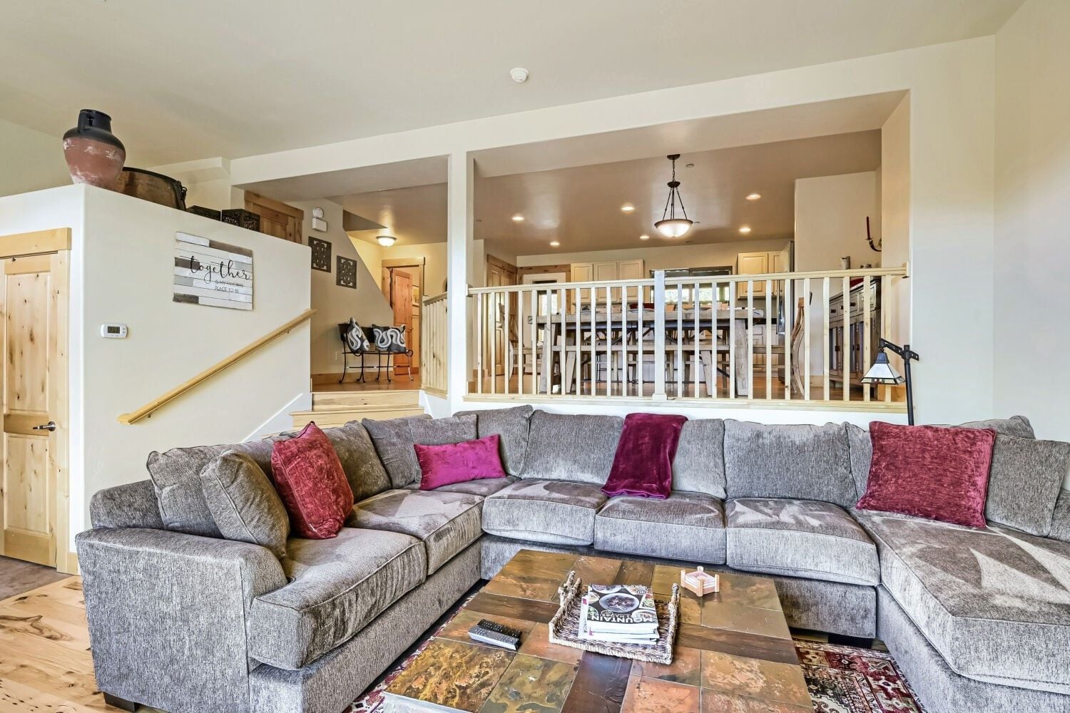 A modern living room with a grey sectional sofa, a coffee table, and a staircase leading to a dining area.