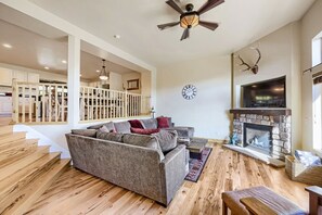 A spacious living room with a fireplace, a staircase leading to an upper level, and a large window providing natural light. - Bear Hollow Beauty. Hottub Walk To Free Bus 5435 5 Bedroom Home (Park City)