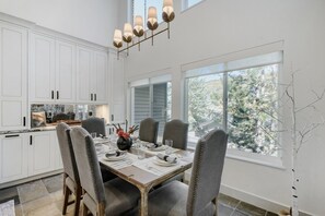 A modern kitchen with white cabinets, a dining table set for four, and large windows offering a view of trees. - Deer Valley Ski Retreat Hot Tub & Fire Pit 1111 2 Bedroom Home (Park City)
