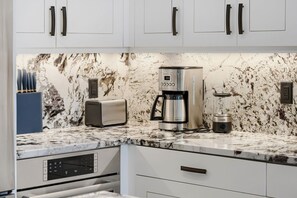 A modern kitchen with white cabinets, a marble countertop, a coffee maker, a toaster, and a blender. - Deer Valley Ski Retreat Hot Tub & Fire Pit 1111 2 Bedroom Home (Park City)