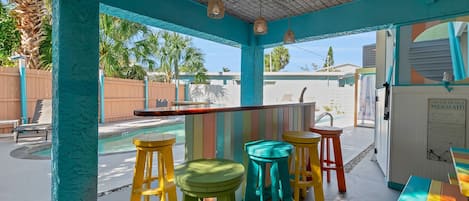 A covered outdoor area with a pool, colorful stools, and a table.