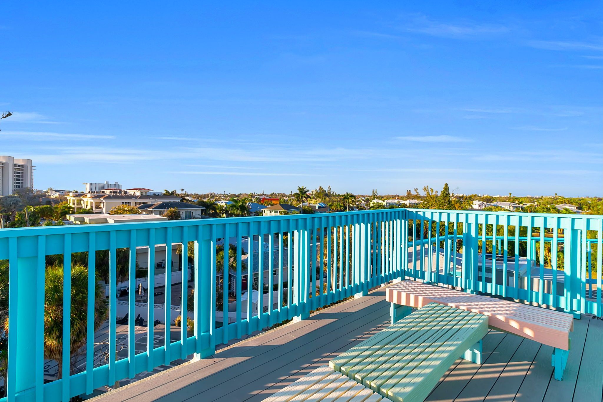 A blue outdoor deck with a bench and a view of a residential area.