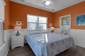 A bedroom with a bed, nightstands, a window with blinds, a ceiling fan, and a bathroom with a toilet and sink. - Siesta Sunset Royale #5 2 Bedroom Apts (Siesta Key)