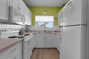 A kitchen with white cabinets, a stove, a sink, and a window with a view. - Siesta Sunset Royale #45 3 Bedroom Apts (Siesta Key)