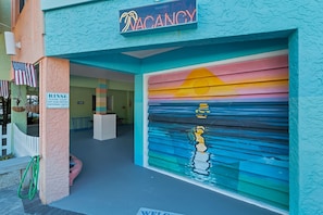 A building with a closed garage door, a sign indicating a vacancy, and a sign requesting guests to clean off sand before entering. - Siesta Sunset Royale #45 3 Bedroom Apts (Siesta Key)
