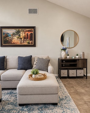 A living room with a sofa, ottoman, and a side table with decorative items. - Private Pool Home - 12 Min to UCF - Sleeps 4 - Near Orlando Parks (Oviedo)
