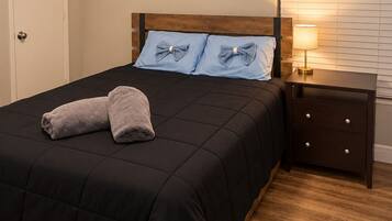 A bedroom with a bed, pillows, a bedside table with a lamp, a door, and a wall with a painting.