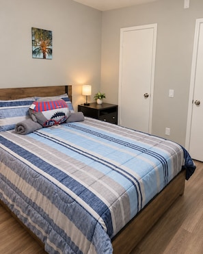 A neatly made bed with a striped bedspread, a pillow with a shark design, and a bedside lamp. - Private Pool Home - 12 Min to UCF - Sleeps 4 - Near Orlando Parks (Oviedo)
