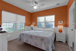 Une chambre à coucher comprenant un lit, deux tables de chevet, un ventilateur de plafond et des fenêtres équipées de stores.