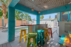 A covered outdoor area with a pool, colorful stools, and a table. - Siesta Sunset Royale #456 4 Bedroom Apts (Siesta Key)