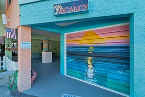 A building with a closed garage door, a sign indicating a vacancy, and a sign requesting guests to clean off sand before entering. - Siesta Sunset Royale #456 4 Bedroom Apts (Siesta Key)