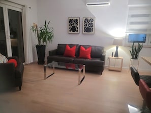 A living room with a sofa, a coffee table, a potted plant, and artwork on the wall. - Walk Kingsville !! 2 to 7 minute walk to all the great spots ! 8 People (Kingsville)