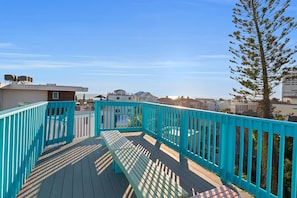 Eine Holzterrasse mit einer türkisblauen Reling, mit Blick auf eine Wohngegend mit Häusern und einem klaren Himmel.