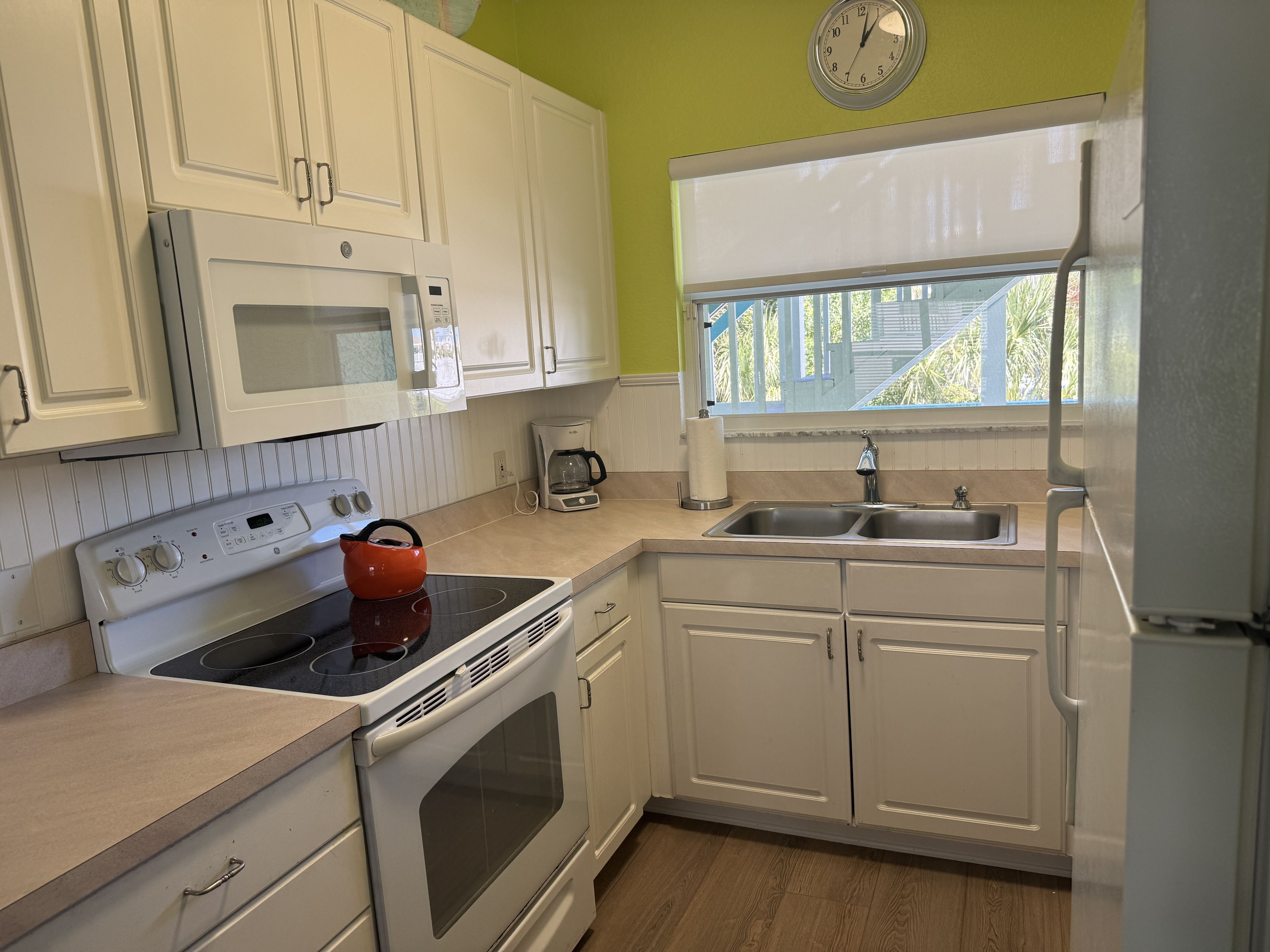 A kitchen with white cabinets, a microwave, a stove, a coffee maker, and a sink.