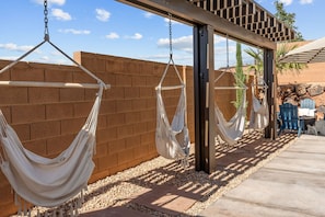 A series of white hammocks suspended from a wooden structure against a brick wall, with outdoor furniture and a clear sky in the background. - Prospector Peaks 5 Bedroom Home (Washington)