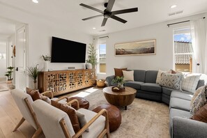 A modern living room with a flat-screen TV, a sectional sofa, leather ottomans, a wooden coffee table, and a ceiling fan. - Prospector Peaks 5 Bedroom Home (Washington)