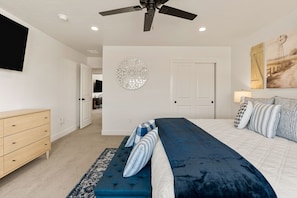 A bedroom with a bed, a dresser, a ceiling fan, a wall-mounted TV, and a door leading to another room. - Prospector Peaks 5 Bedroom Home (Washington)