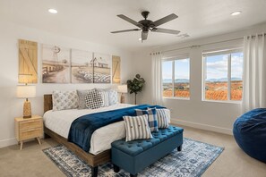 Ein Schlafzimmer mit einem Bett, einer blauen Bank, einem Deckenventilator und einem großen Fenster mit Blick.