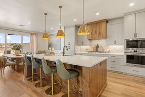 Een moderne keuken met een centraal eiland, barkrukken, hanglampen en roestvrijstalen apparatuur.