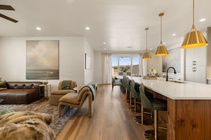 A modern kitchen with a bar area, wooden flooring, and pendant lighting. - The Desert Isle 5 Bedroom Townhouse (Washington)