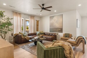 Een moderne woonkamer met een bruine leren bank, een groene fauteuil, een salontafel en een groot schilderij aan de muur.