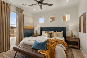 Een slaapkamer met een groot bed, een plafondventilator, uitzicht op de omgeving en een raam met gordijnen.
