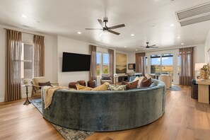 A spacious living room with a large round sofa, a flat-screen TV mounted on the wall, and a ceiling fan. - The Desert Isle 5 Bedroom Townhouse (Washington)