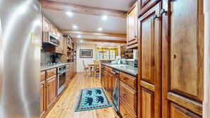 A kitchen with wooden cabinets, stainless steel appliances, and a dining area with a table and chairs. - Sierra Megeve #29 3 Bedroom Condo (Mammoth Lakes)