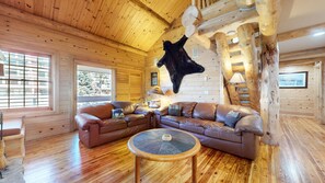 A log cabin interior with a leather sofa, a round wooden table, and a mounted animal hide. - Sierra Megeve #29 3 Bedroom Condo (Mammoth Lakes)