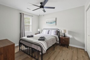 Ein Schlafzimmer mit einem Bett, Nachttischen, einem Deckenventilator, einem Fenster mit Vorhängen und einem Gemälde an der Wand.