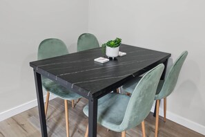Uma mesa de jantar retangular com tampo de mármore preto, rodeada por quatro cadeiras estofadas verdes com pés de madeira.