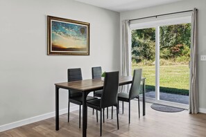 Ein Essbereich mit Tisch und Stühlen, einem Bild an der Wand und Blick auf Grün durch eine Glastür.