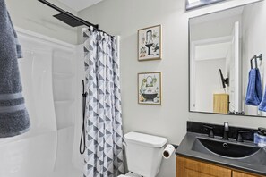 Ein Badezimmer mit Duschvorhang, Toilette, Waschbecken und zwei gerahmten Bildern an der Wand.