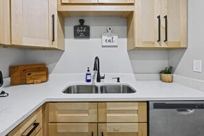 A kitchen with wooden cabinets, a stainless steel sink, a dish soap bottle, and a potted plant. - Newly Renovated 2BR/2BA | Workspace + 3 TVs (Calhoun)