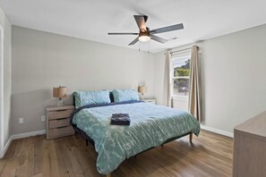 Ein Schlafzimmer mit einem Bett, Nachttischlampen, einem Deckenventilator und einem Fenster mit Vorhängen.