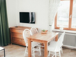 A dining area with a wooden table and white chairs, a television on the wall, and a window with curtains. - House Luna - Apartment Luna 2 (Schwangau)