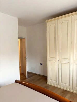 Habitació amb un armari ampli, un paviment de fusta i una porta que dona a una altra habitació.
