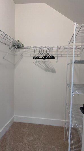 A corner of a room with a white wall, a beige carpet, and a metal shelving unit with clothes hangers. - The Best Place for Family Stays, and Small Group (Mint Hill)