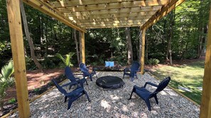 A covered outdoor seating area with four chairs and a round table, surrounded by gravel and greenery. - The Best Place for Family Stays, and Small Group (Mint Hill)