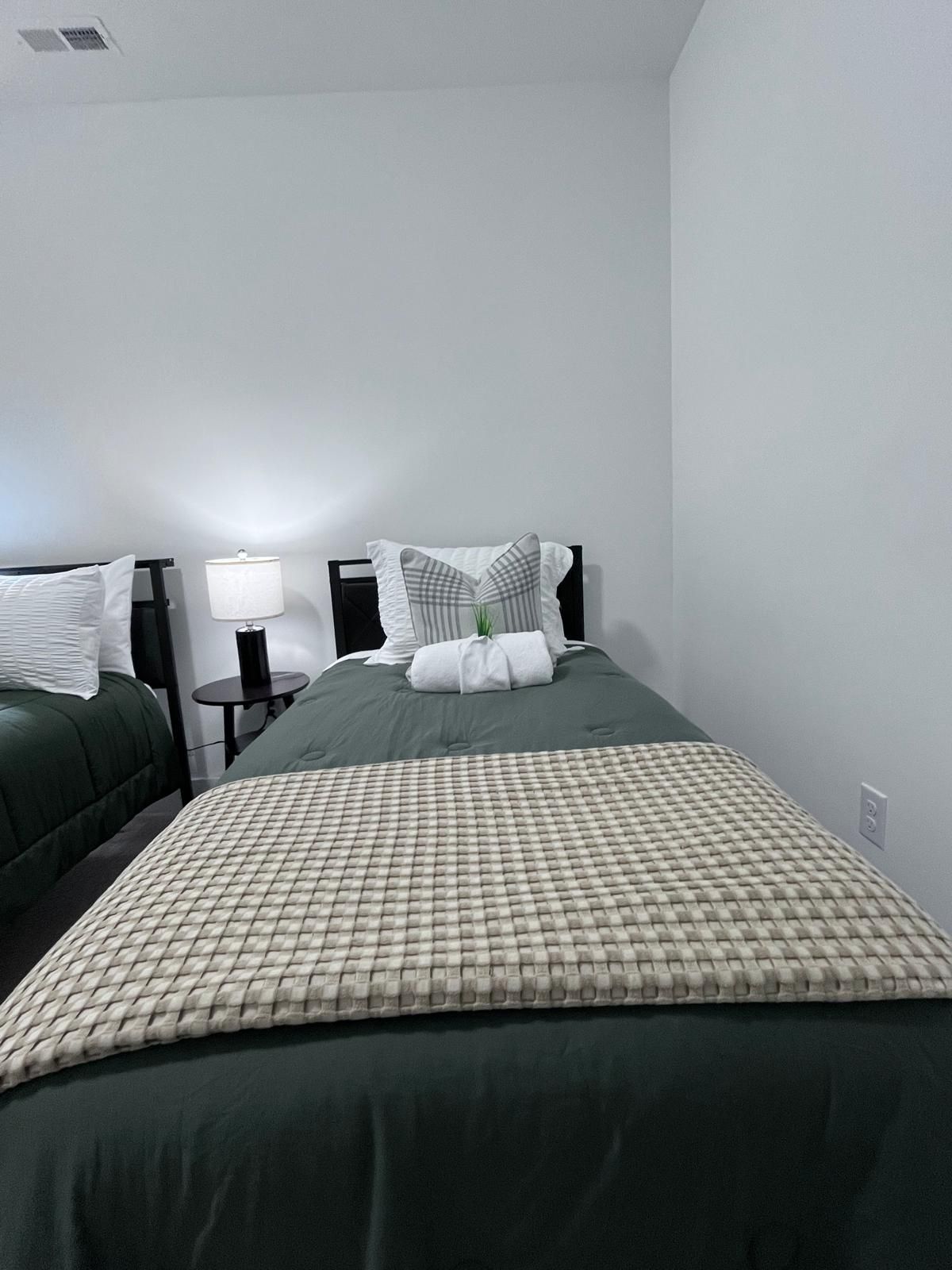 Une chambre d’hôtel avec deux lits, une table de chevet avec une lampe et une bouche d’aération fixée au mur.