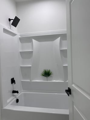 Une salle de bain moderne avec une baignoire, des étagères et une petite plante.