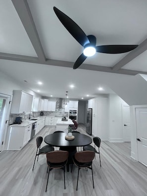 Une cuisine moderne avec des meubles blancs, un îlot central et un ventilateur de plafond.