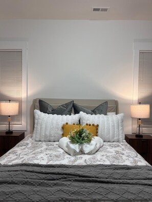Un lit bien fait, recouvert d’une couvre-lit à motifs floraux, avec deux lampes de chevet et un élément décoratif au centre.