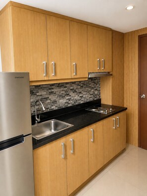 A modern kitchen with wooden cabinets, a stainless steel refrigerator, a black countertop, and a tiled backsplash. - Quaint 1BR Condo Terrace-pool View Moa-shell (Pasay)