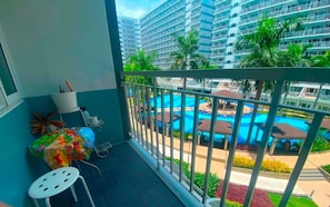 A balcony with a view of a swimming pool and a high-rise building. - Quaint 1BR Condo Terrace-pool View Moa-shell (Pasay)