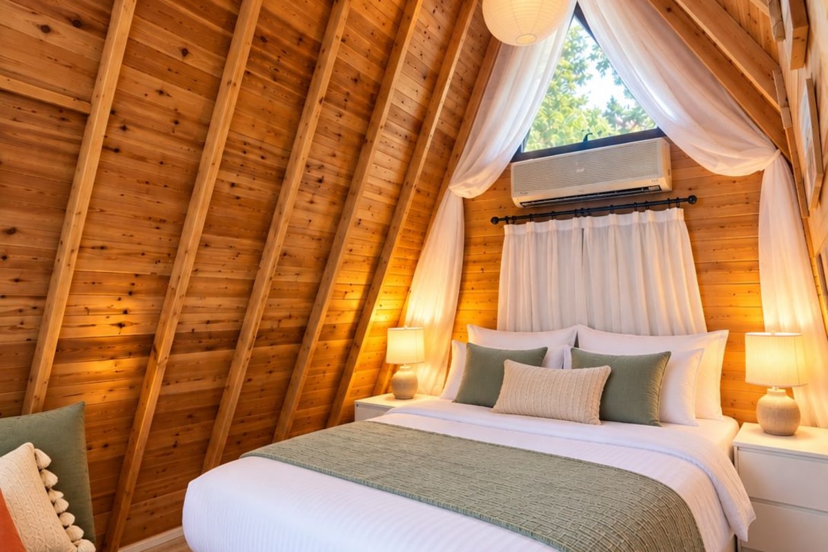 Una stanza di legno accogliente dalla forma triangolare, con un letto, comodini e una finestra con tende.